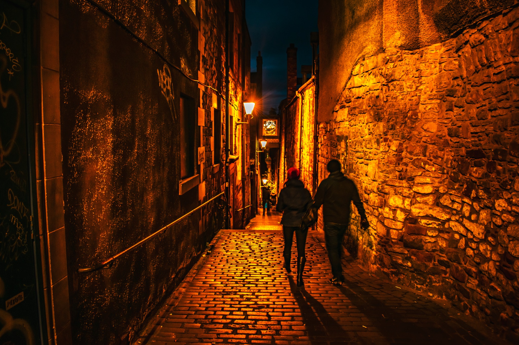 A couple walking through a warmly lit historic Edinburgh close